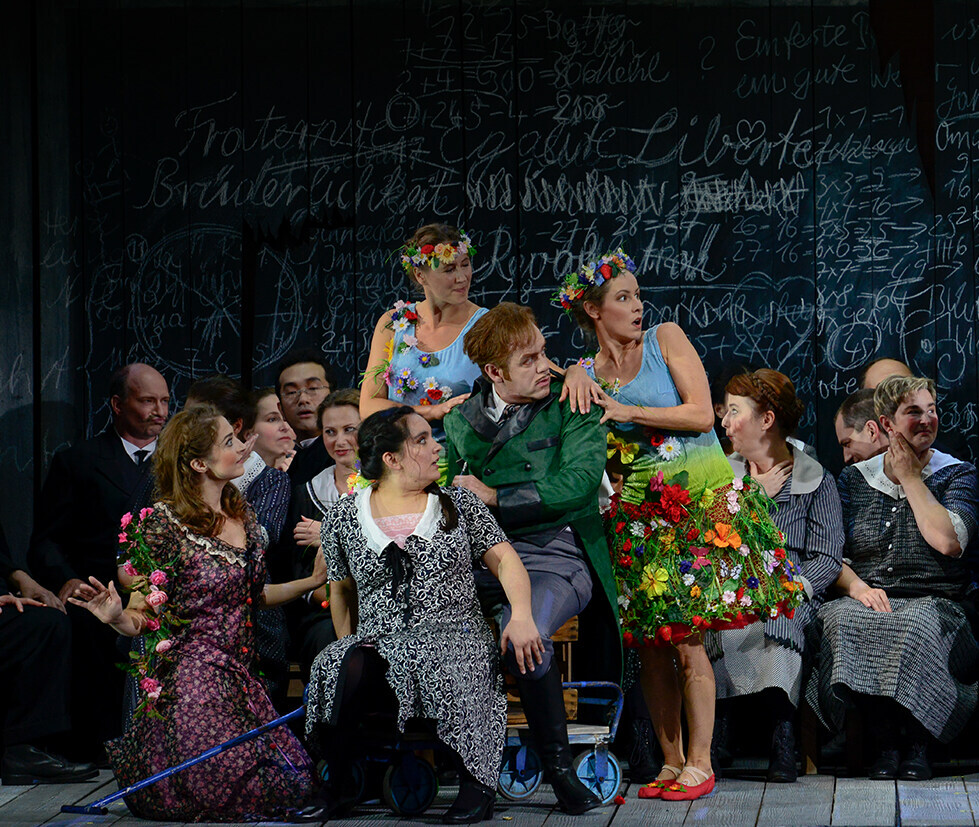 Szene aus "Der Wildschütz": Recht und links sind zwei Sänger, der rechts Sitzende ist umringt von 4 Sängerinnen